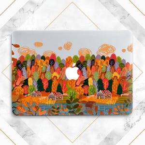 May include: A laptop skin with a colorful autumn forest scene. The design features a variety of trees with orange, yellow, red, and green leaves. There are two small cabins in the foreground, and a lake in the middle ground. The skin is designed to fit a MacBook.