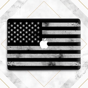 Puede incluir: Piel de portátil negra con un diseño de bandera estadounidense blanca desgastada y un logotipo de Apple blanco.