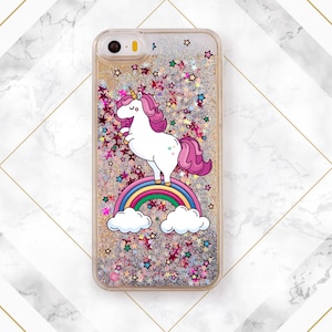 May include: A clear phone case with a glittery background and a unicorn standing on a rainbow. The unicorn is pink and white with a pink mane and tail. The rainbow is multi-colored with clouds on either side.