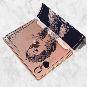 Może przedstawiać: Etui na iPada w kolorze r&oacute;żowego złota z czarno-białym rysunkiem twarzy kobiety z kwiatowymi detalami. Etui ma czarny symbol pika i napis "Queen of Hearts".