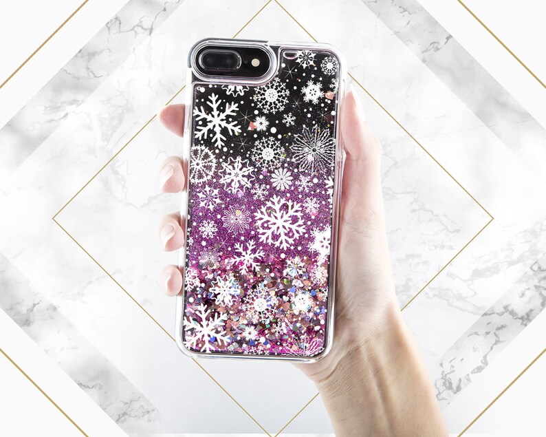 May include: A clear phone case with a glittery pink and white design featuring snowflakes. The case is made of a clear plastic material and has a raised lip around the edges to protect the screen.