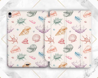 Può includere: Una custodia per tablet color crema con un motivo ripetuto di varie conchiglie nei toni dell'arancione, rosa, verde, blu e viola. La custodia è aperta, mostrando il design interno ed esterno. Il tema generale è costiero e nautico.