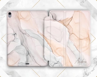 May include: A tablet case with a marble design in shades of blush, gray, and beige. The case is open, revealing the interior. The name "Andrea" is written in cursive on the front cover. The case is designed to protect a tablet.