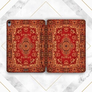 Peut inclure: Un étui pour tablette pliable arborant un motif de tapis oriental complexe dans des tons rouge et or. Le design présente un médaillon central entouré de bordures florales et géométriques détaillées, avec une découpe pour appareil photo.