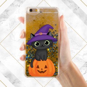 May include: A clear phone case with a gold glitter background and a black cat wearing a purple witch hat sitting on a jack-o-lantern.