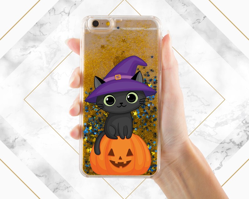 May include: A clear phone case with a gold glitter background and a black cat wearing a purple witch hat sitting on a jack-o-lantern.