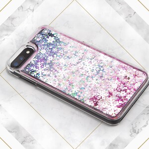 May include: A clear phone case with a pink, white, and blue glitter design. The glitter is shaped like snowflakes and is moving around inside the case.