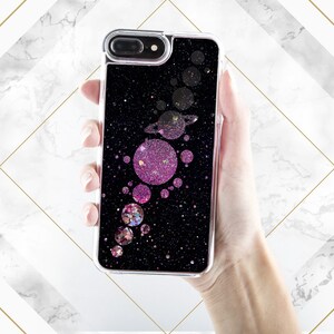 May include: A black phone case with a glittery design featuring pink and gold circles and a galaxy-like background.