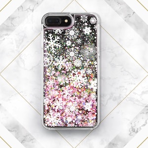 May include: A clear phone case with a glittery pink and white snowflake design. The case is designed for an iPhone.