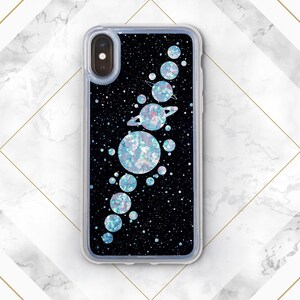 May include: A black phone case with a glitter background and a design of planets and stars. The planets are iridescent and have a sparkly finish.