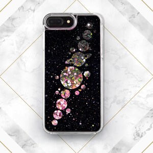 May include: A clear phone case with a black background and pink and silver glitter. The glitter is arranged in a pattern of planets and stars.