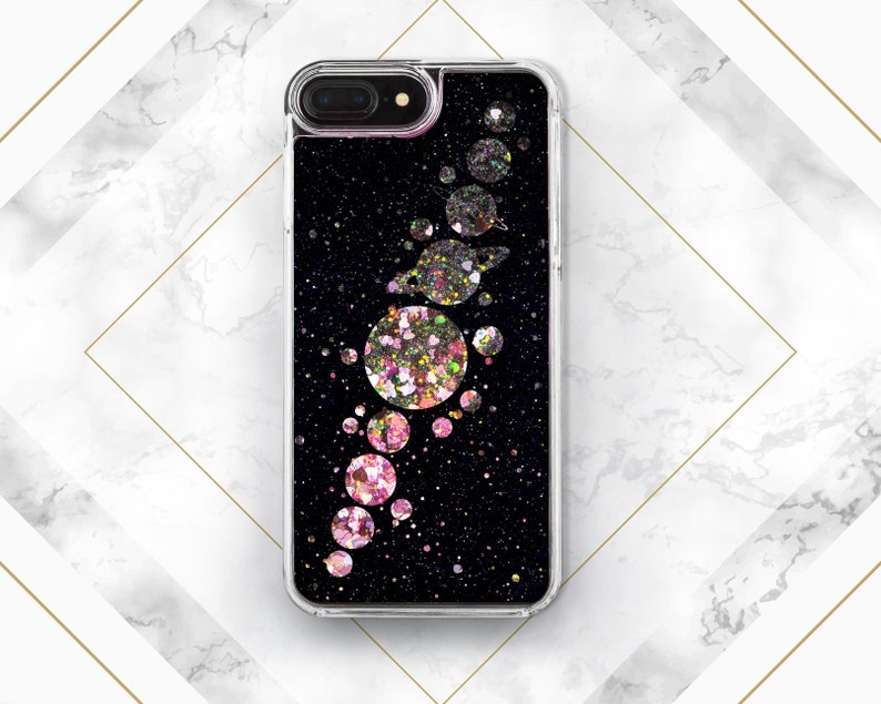 May include: A clear phone case with a black background and pink and silver glitter. The glitter is arranged in a pattern of planets and stars.