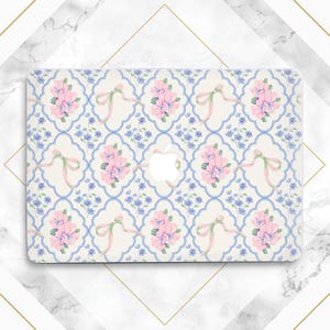 May include: A white laptop case with a floral pattern. The pattern features pink flowers, blue leaves, and white ribbons on a cream background.