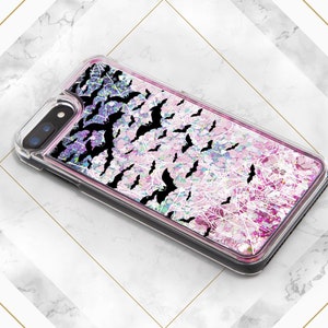 May include: A clear phone case with a pink and purple glitter background. The case has a black spiderweb design and black bats flying around the web.