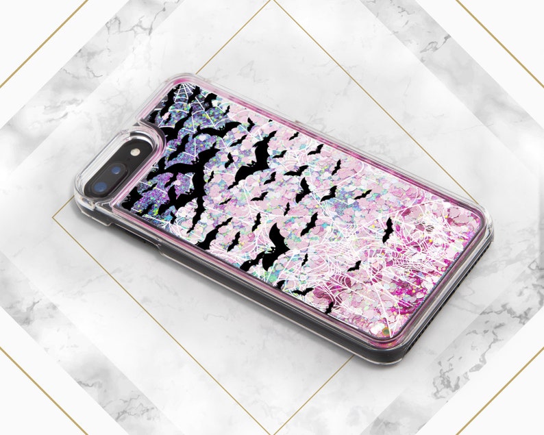 May include: A clear phone case with a pink and purple glitter background. The case has a black spiderweb design and black bats flying around the web.