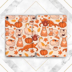 May include: A phone case with a pattern of orange and white cats, pumpkins, and autumn leaves. The case is designed for a phone with a flip cover.
