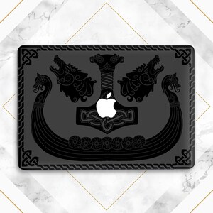 May include: A black laptop case featuring a Viking design. The design includes a longboat, snarling wolves, a hammer, and Celtic knot patterns. The Apple logo is visible in the center of the case.