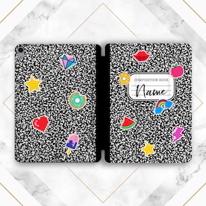 May include: A black and white composition book cover with a variety of colorful stickers, including a donut, a watermelon, a rainbow, a lightning bolt, a star, a heart, a diamond, an apple, a popsicle, and a red lip. The cover also has a white label that says "Composition Book" and "Name".