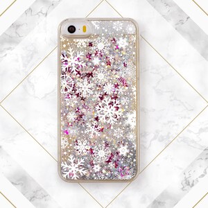 May include: A clear phone case with a glittery background and white snowflake designs. The case has a gold trim around the edges.