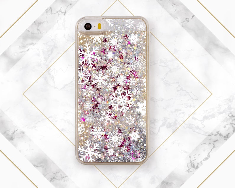 May include: A clear phone case with a glittery background and white snowflake designs. The case has a gold trim around the edges.