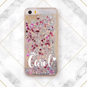 May include: A clear phone case with a glittery background and pink stars. The case has a white crown and the name "Carol" with a pink heart.