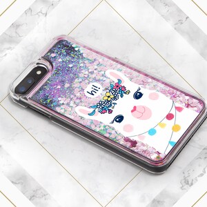 May include: A clear phone case with a pink, purple, and white glitter background. A white llama with a pink nose and a flower crown is featured on the case. The llama has a speech bubble that says "hi!"