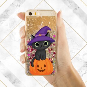 May include: A black cat wearing a purple witch hat sits on top of an orange pumpkin with a carved jack-o'-lantern face. The image is on a gold glitter phone case.
