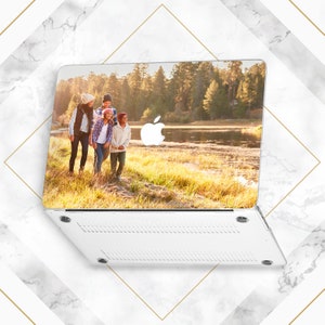 May include: A white laptop case featuring a photograph of a family of four walking in a grassy field by a lake. The image is printed on the top of the case, and the bottom of the case is white with a textured design.