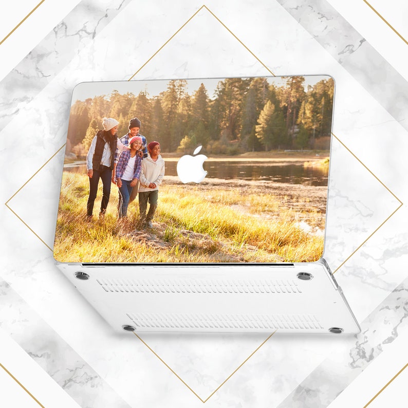 May include: A white laptop case featuring a photograph of a family of four walking in a grassy field by a lake. The image is printed on the top of the case, and the bottom of the case is white with a textured design.