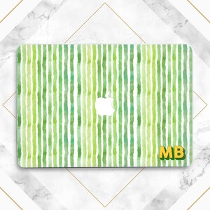 Op de afbeelding: Een laptop skin met een aquarelontwerp van verticale groene strepen op een witte achtergrond. Het Apple-logo is zichtbaar in het midden. De initialen "MB" staan in geel en groen rechtsonder.