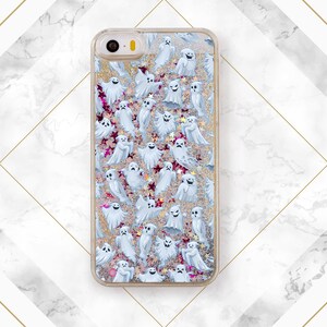 Puede incluir: Una funda de tel&eacute;fono transparente con un fondo brillante y un patr&oacute;n de fantasmas blancos. Los fantasmas est&aacute;n en varias poses y tama&ntilde;os.