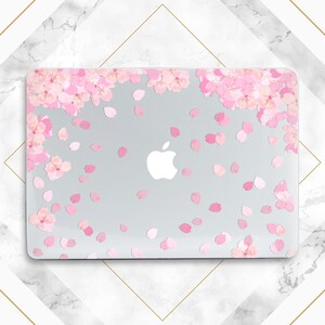 Puede incluir: Una funda transparente para portátil con un diseño de flores de cerezo rosas. La funda tiene un logotipo de Apple blanco en la parte delantera.