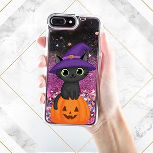 May include: A black cat wearing a purple witch hat sits on a carved orange pumpkin. The image is inside a clear phone case with pink and black glitter.