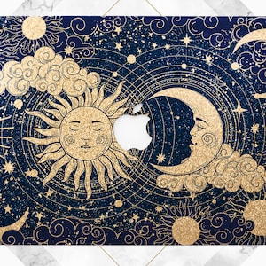 May include: A navy blue laptop skin with a gold glitter design featuring a sun, moon, and stars. The design is reminiscent of a celestial night sky.