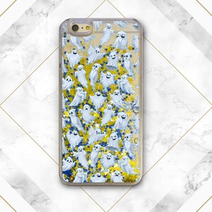 Puede incluir: Una funda de tel&eacute;fono transparente con un dise&ntilde;o de fantasmas blancos y purpurina dorada sobre un fondo azul.