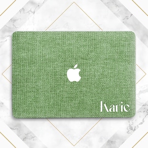 May include: Green laptop cover with a textured fabric design. A white Apple logo is centered, and the name "Karie" is printed in white on the lower right corner. The cover is rectangular and designed to fit a laptop.