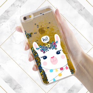 May include: A clear phone case with a gold glitter background and a white llama with a floral crown and the word "hi!" in a speech bubble.