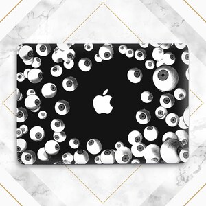 May include: Black laptop skin featuring a pattern of white, detailed eyeballs against a black background. A white Apple logo is centered. The design is a unique and eye-catching accessory.
