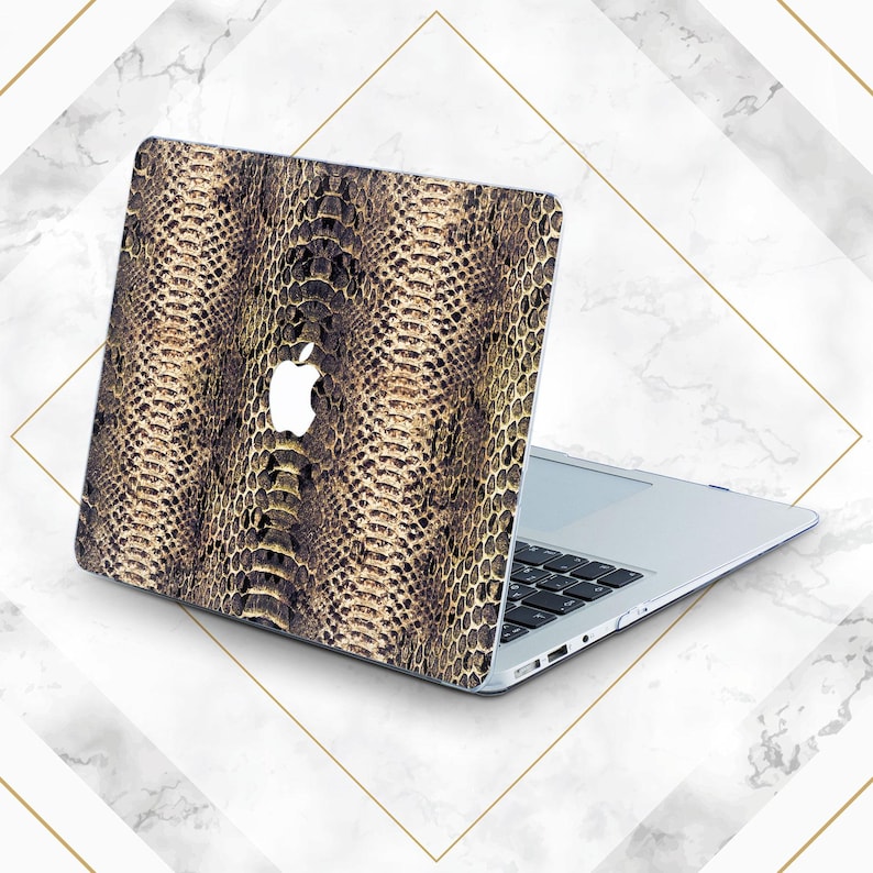 May include: A laptop computer with a snakeskin pattern on the lid. The laptop is closed and the lid is open at an angle. The laptop is on a white marble surface.