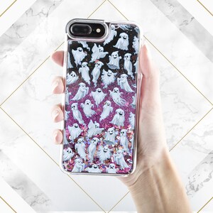 Puede incluir: Una funda transparente para tel&eacute;fono con un fondo de purpurina rosa y blanca y un patr&oacute;n de fantasmas blancos.