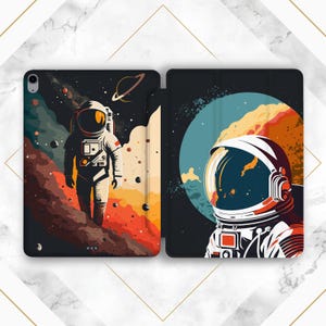 May include: A black and white illustrated iPad case featuring an astronaut in a spacesuit against a colorful space background. The case is open, displaying the full design with a planet and stars.