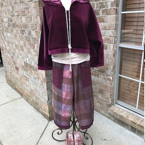 May include: A quilted burgundy velvet hooded jacket with a pearl necklace and a pair of plaid pants with a brown and purple color scheme. The pants are on a decorative stand and the jacket is on a mannequin.
