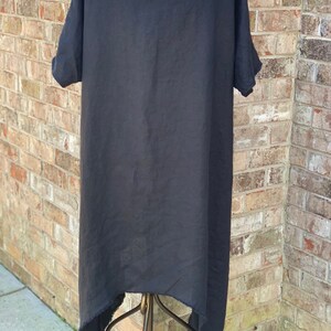 May include: Black linen dress with a high low hemline and short sleeves. The dress is hanging on a gold stand.
