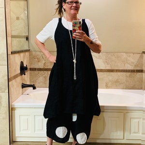 Może przedstawiać: Kobieta w czarnej lnianej sukience z białymi spodniami w kropki i czarnymi butami Converse. Stoi w łazience z białą wanną i kafelkowaną ścianą.