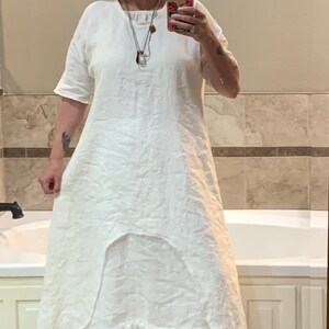 May include: A white linen dress with a ruffled hem and a scoop neck. The dress is worn with a straw hat and strawberry print sneakers.