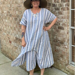 May include: A woman wearing a blue and white striped dress with a wide-brimmed straw hat, a necklace, and gray sneakers.