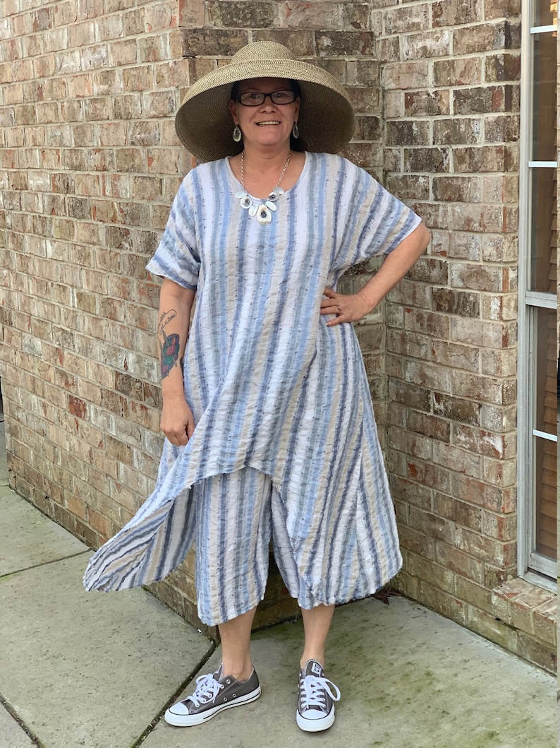May include: A woman wearing a blue and white striped dress with a wide-brimmed straw hat, a necklace, and gray sneakers.