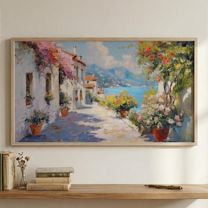 May include: Oil painting depicting a coastal street scene with white buildings, terracotta flower pots, and a view of the blue sea and mountains. The artwork is framed in a light wood frame.