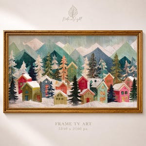 May include: A framed artwork depicting a winter village scene. Colorful houses are nestled among snow-covered ground and evergreen trees, with mountains in the background. The artwork is framed in a gold-colored rectangular frame. The text "FRAME TV ART 3840 x 2160 px" is at the bottom.