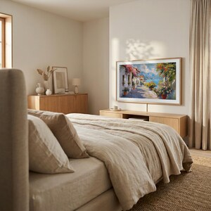 May include: A bedroom with a large framed painting depicting a coastal town. The painting is mounted above a wooden cabinet. A bed with beige bedding and pillows is in the foreground. The room has neutral tones and natural light.